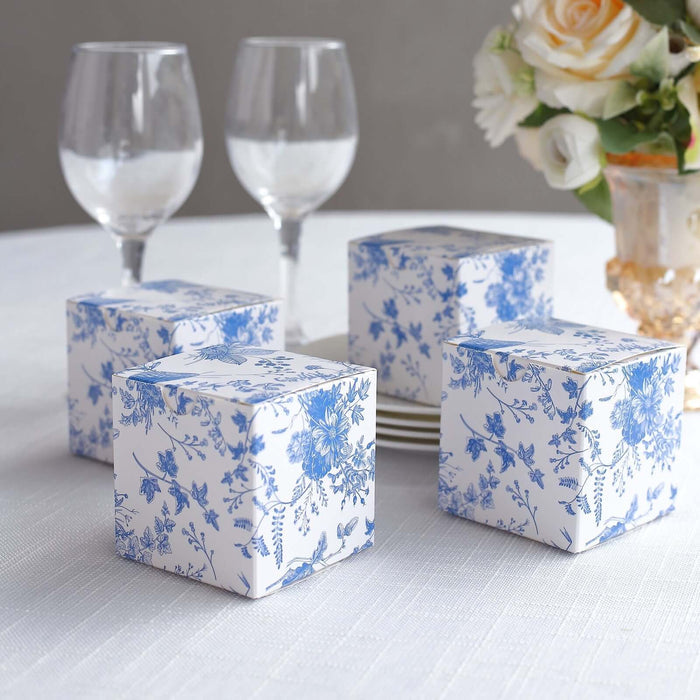 Decorative blue floral gift boxes on a table with glasses and flowers.
