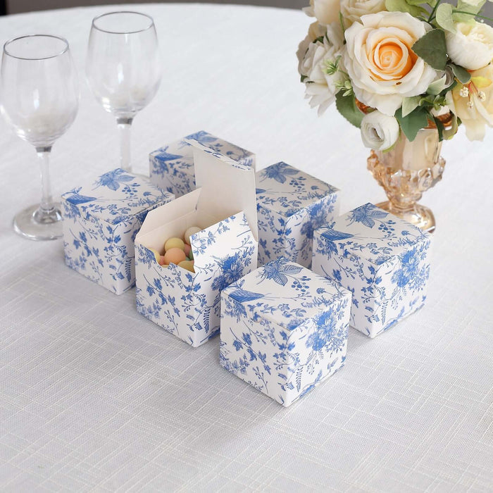 Decorative blue floral gift boxes arranged on a table with glasses and flowers.