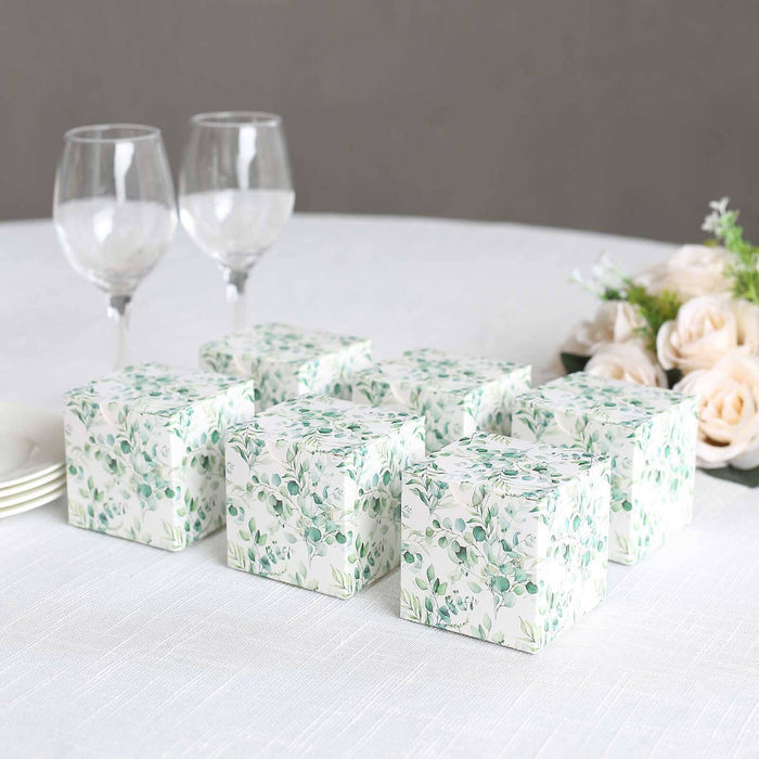 Decorative floral gift boxes on a table with wine glasses and flowers.