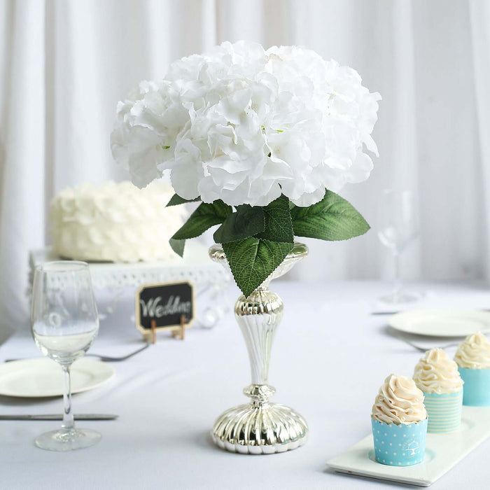 White hydrangea bouquet in a silver vase on a table setting.