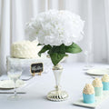 White hydrangea bouquet in a silver vase on a table setting.
