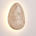 front view of the organic pebble-shaped travertine wall sconce, lit on a plain background
