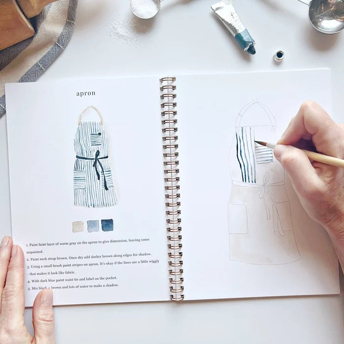Person drawing an apron design in a book with a paintbrush
