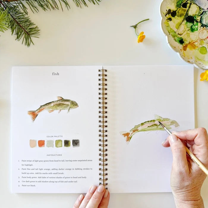 Open book with watercolor illustrations of fish, hand holding a paintbrush, and painting a fish.