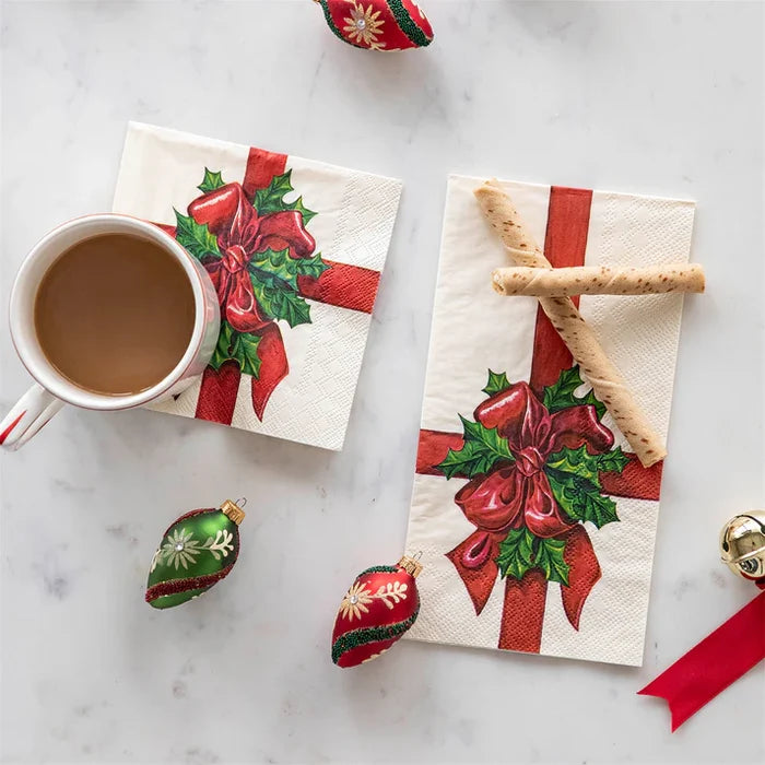 Napkins with Christmas designs featuring red bows and holly leaves, accompanied by a cup of coffee on a marble surface.