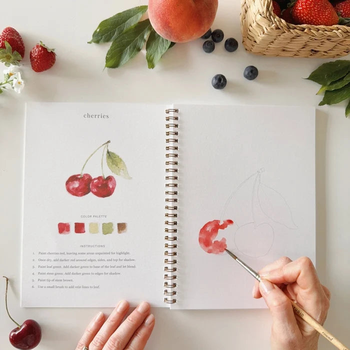 Open notebook with cherry illustration and color swatches, surrounded by fruits