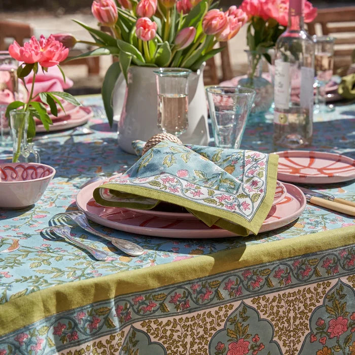 Decorative table setting with blue a green  floral tablecloth, plates, and napkins.