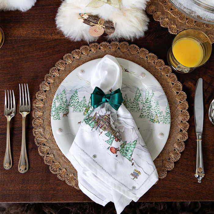 Christmas-themed table setting with decorative plates, napkins, and cutlery on a wooden table.