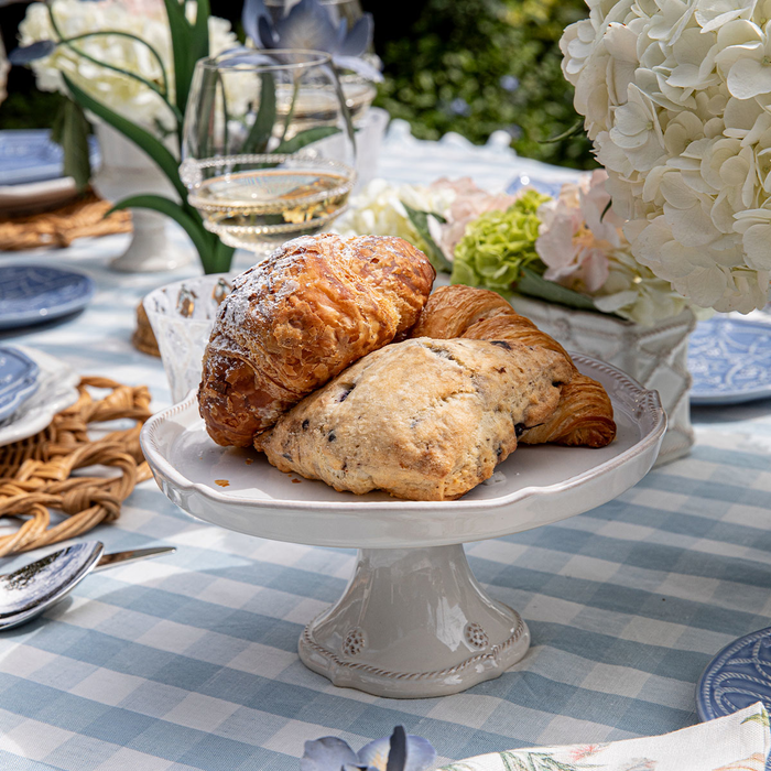 Pastries on a white pedestal plate with a checkered tablecloth and floral decorations in the background.