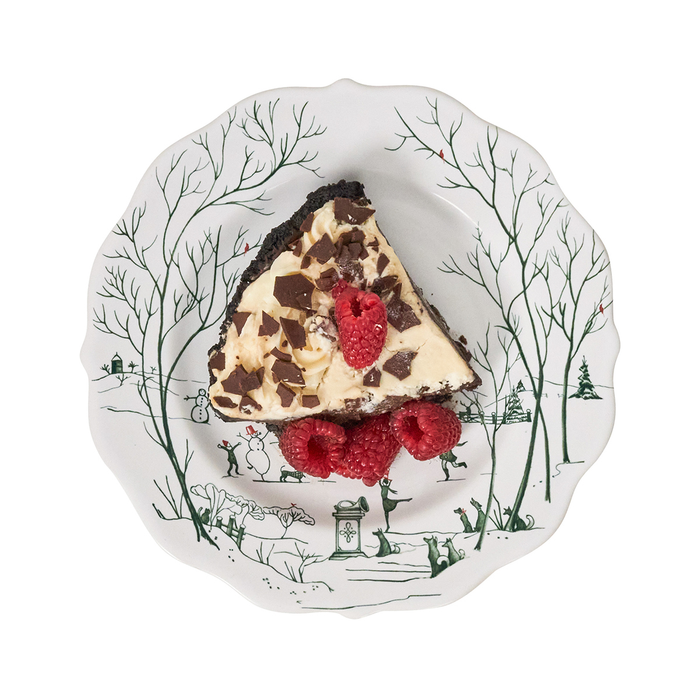 Slice of chocolate chip cheesecake on a white plate with green painted winter scene