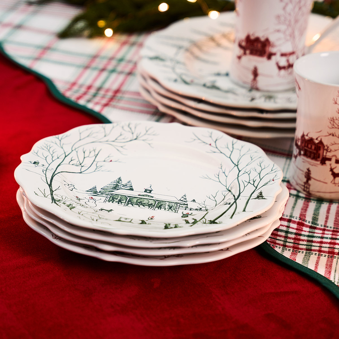 Stack of white plates with a green painted Christmas theme on a red tablecloth.