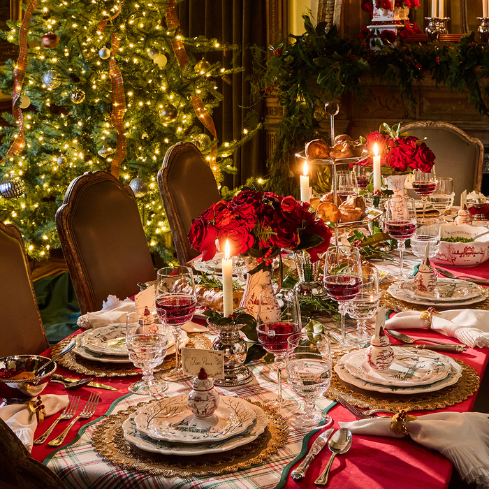 Decorated Christmas table with red flowers, candles, and a lit tree in the background.