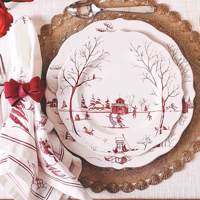 Decorative plate with red winter scene design on a natural fiber placemat next to a white and red holiday napkin tied with a red bow napkin ring