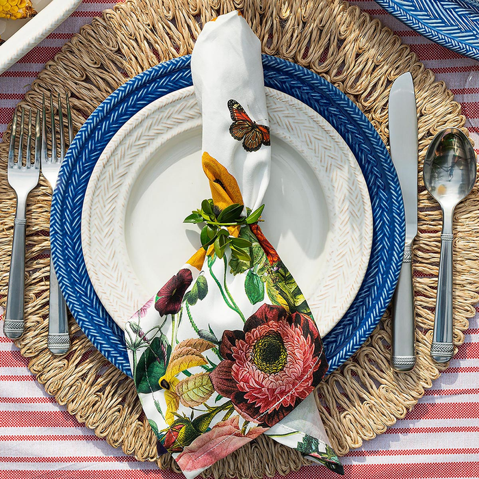 Plated setting with floral napkin, butterfly decoration, and cutlery on a woven placemat.