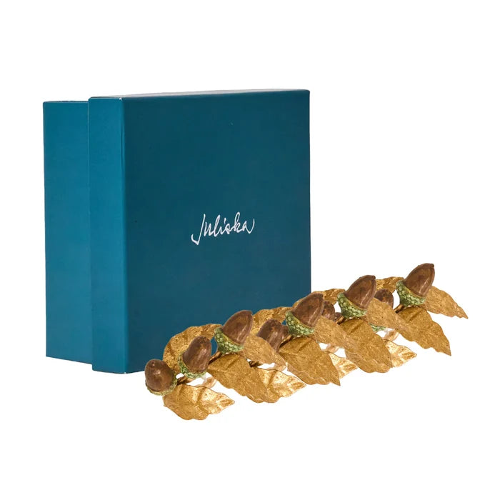 Golden acorn napkin rings laid in front of juliska packaging