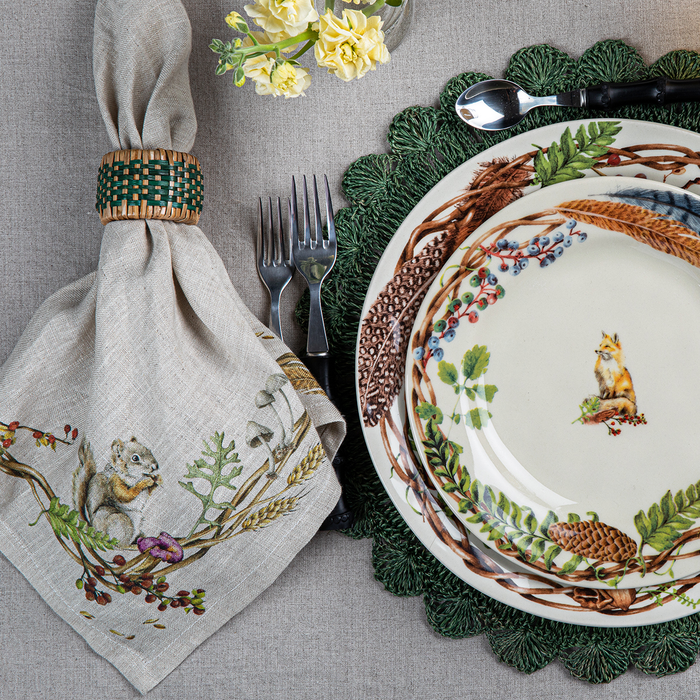 Decorative autumn table setting with plates painted with nature motifs and a fox, napkin with foliage and a squirrel, and cutlery on a textured tablecloth