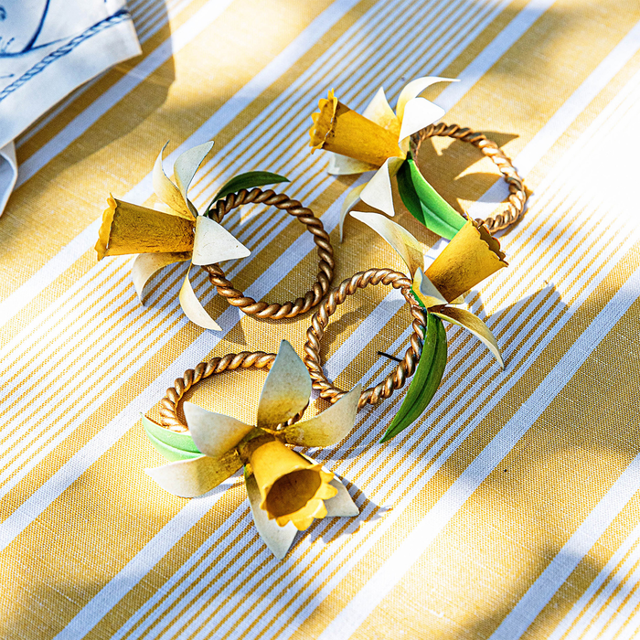 Decorative napkin rings with daffodil sculptures on a striped yellow and white tablecloth.