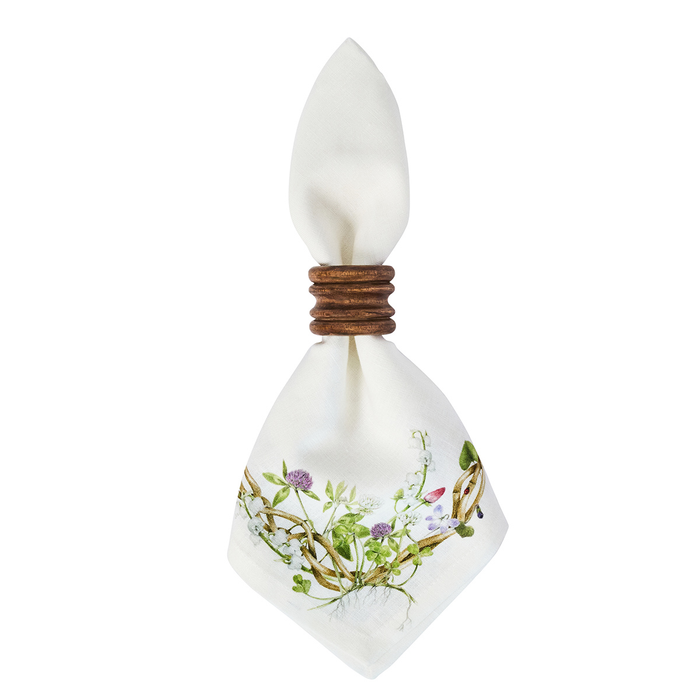 A white square napkin tied with a wooden ring, featuring a delicate botanical illustration of wildflowers and green leaves near the bottom corner