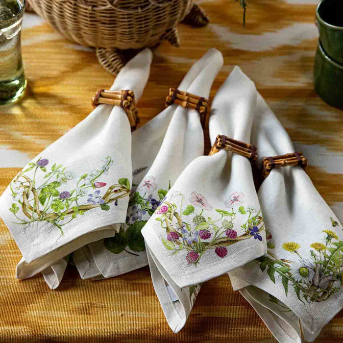 White floral and berry napkins with bamboo napkin rings on a wooden table.
