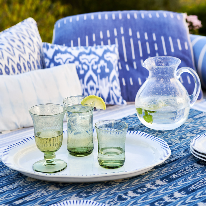 Outdoor setting with green glasses and a pitcher on a blue patterned tablecloth.