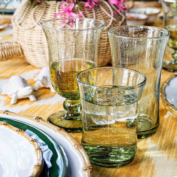 Set of glass green tumblers on a table with a woven basket and decorative items in the background.