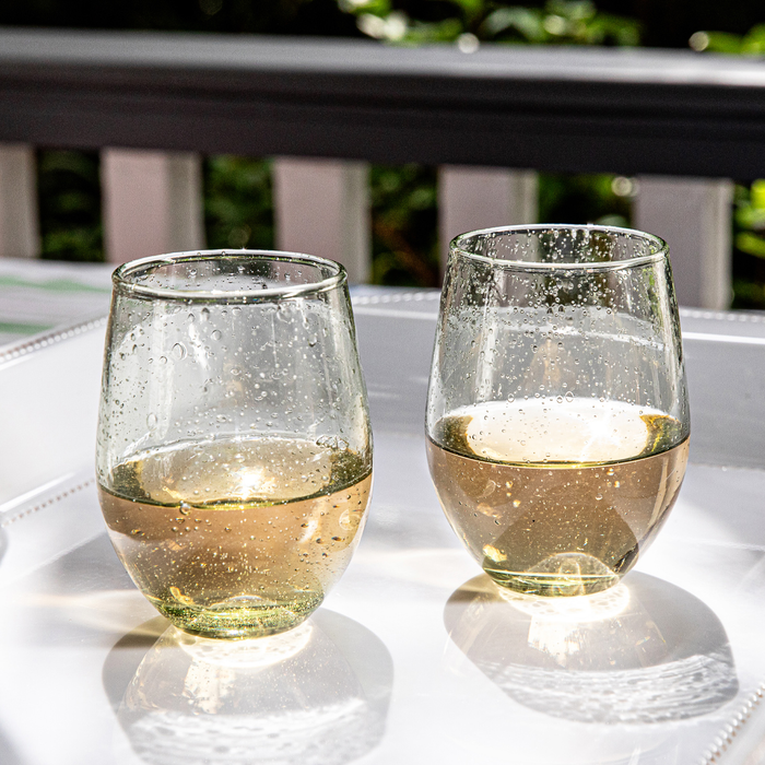 Two green tinted stemless wine glasses filled with white wine on a melamine tray outdoors