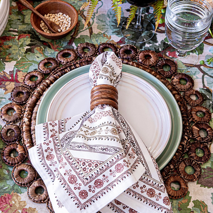Decorative table setting with a patterned napkin and woven charger on a floral tablecloth.
