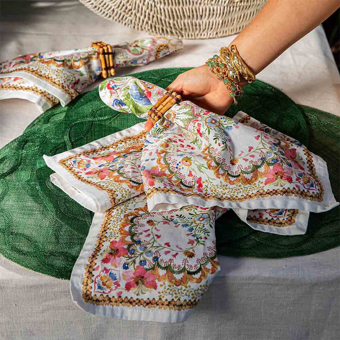 Decorative floral napkins tied with bamboo napkin rings being set onto a green woven placemat