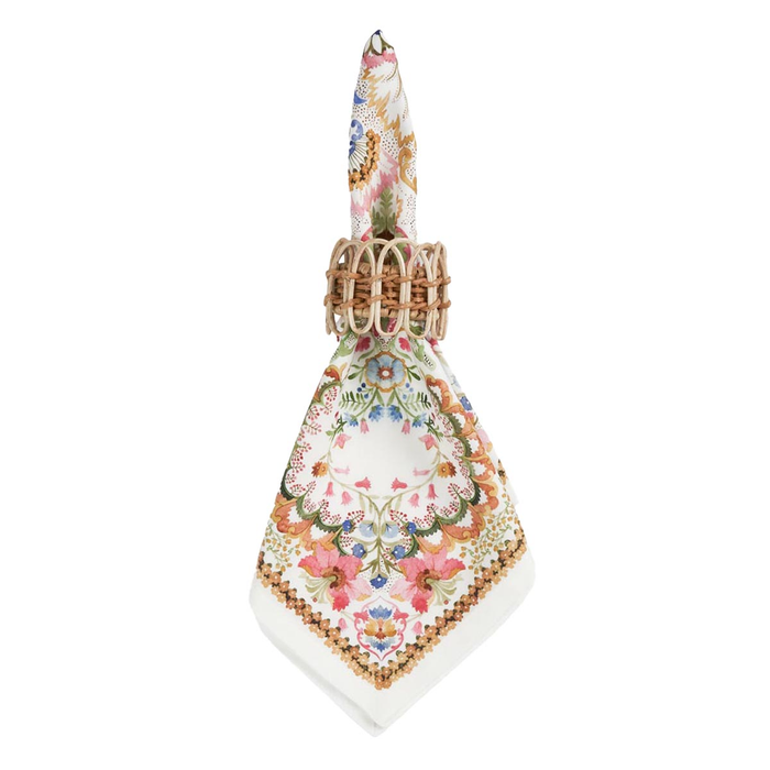 A square napkin with a colorful baroque-style floral and ornamental pattern, featuring a gold-trimmed border with a wicker napkin ring