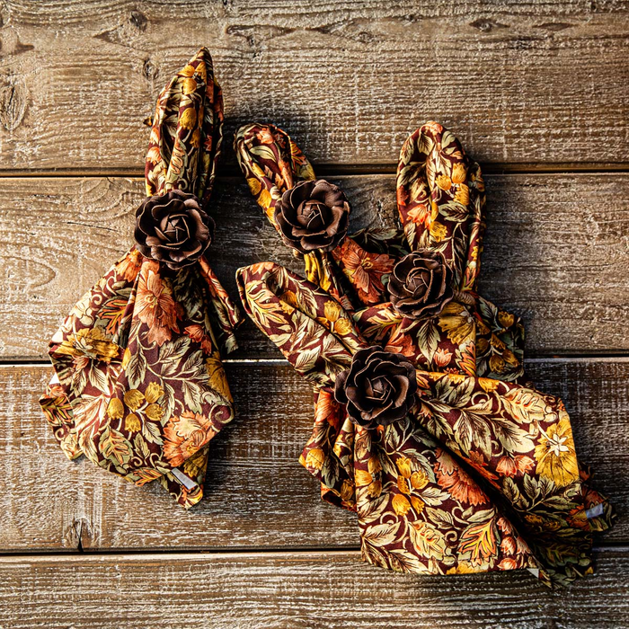 Decorative Autumn floral-patterned napkins tied with flower napkin rings on a wooden surface