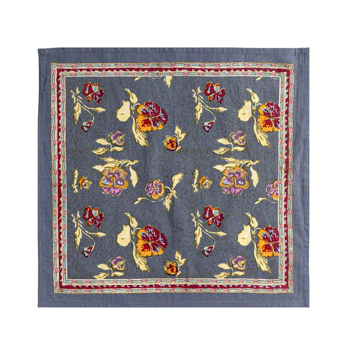 A square blue-gray napkin featuring a colorful floral pattern with red, yellow, and purple flowers, bordered by a red and gold patterned inner frame
