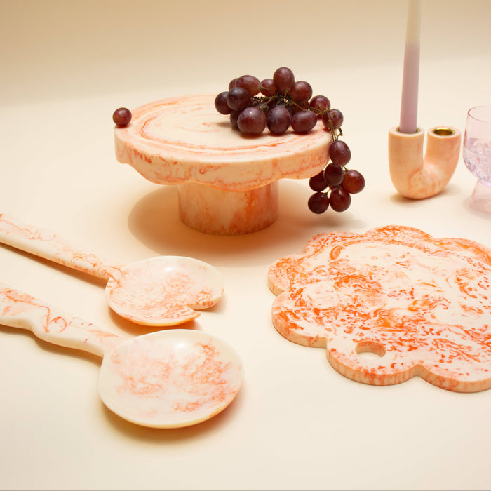 Decorative items including a cake stand with grapes, cookies, and a candle on a beige surface.