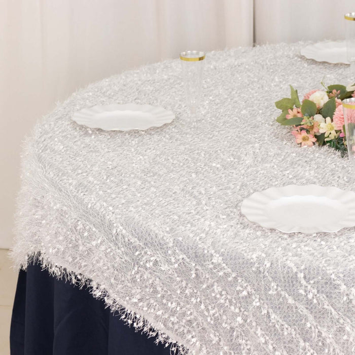 Textured white tablecloth draped over a round table with plates and floral decor.