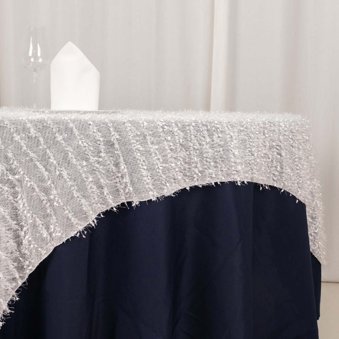 Silver fringe tablecloth on a navy table with a glass and napkin