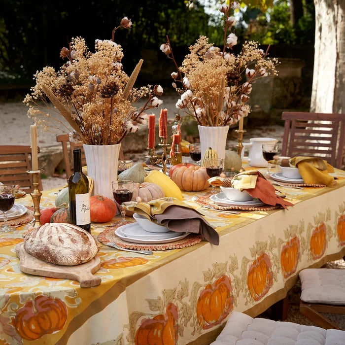 Decorated outdoor table with fall-themed tablecloth, pumpkins, and candles.