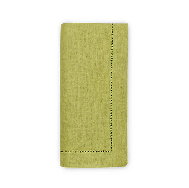 A green linen dinner napkin with hand thread drawn hemstitching on the edge, displayed on a neutral background.