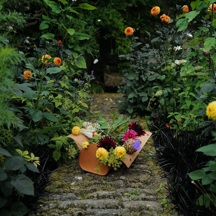 Floral arrangement in a leather garden bag on a stone path surrounded by greenery