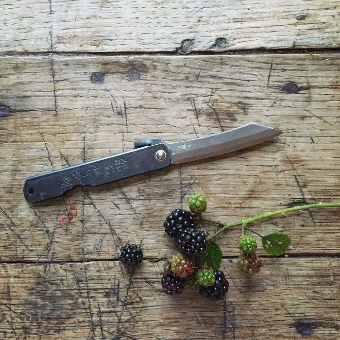 Folding knife on a wooden surface with blackberries and green berries.