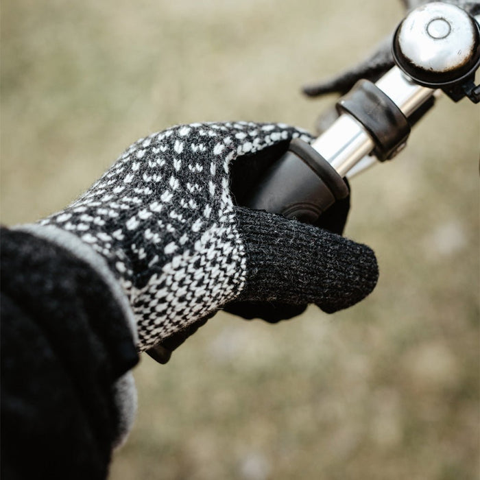 Hand wearing wool mitten holding bicycle handle.