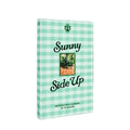 A book titled 'Sunny Side Up' with a mint green and white gingham patterned cover, featuring a small central photograph and the Flamingo estate logo at the top.